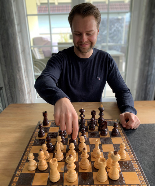 Mann spielt lächelnd an einem Schachbrett.