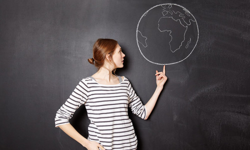 Woman standing in front of a chalkboard pointing to a drawing of the Earth
