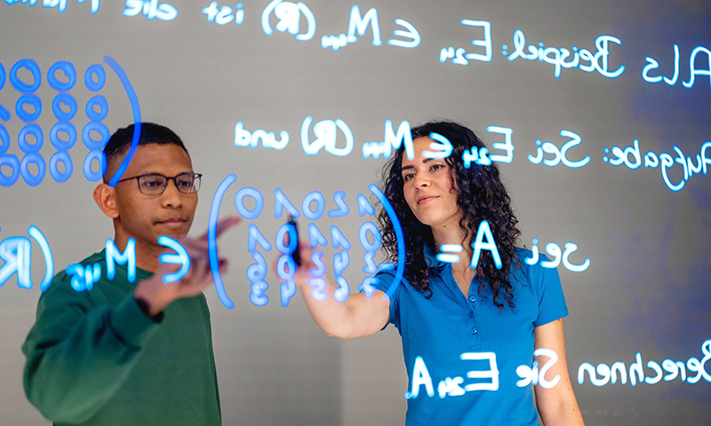 Ein Mann und eine Frau schreiben mathematische Formeln auf einer Schreibtafel