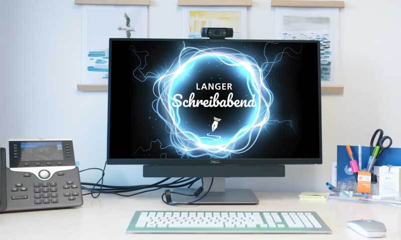 Schreibtisch mit einem Computerbildschirm. Auf dem Bildschirm ist der Schriftzug Langer Schreibabend zu sehen. 