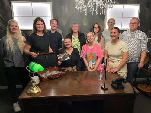 Das Lehrstuhteam steht im Escape Room Enigma gemeinsam hinter einem Schreibtisch.