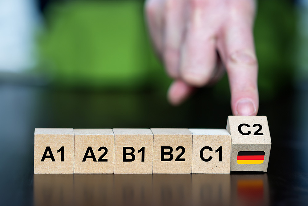 Eine Reihe von fünf Würfeln mit der Beschriftung A1 bis C1, ein Finger kippt den sechsten Würfel mit der Beschriftung C2 an, so dass eine Deutschland-Flagge zu sehen ist.