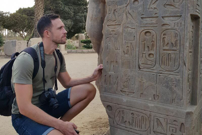 Junger Mann in der Hocke betrachtet Tafel mit Hieroglyphen