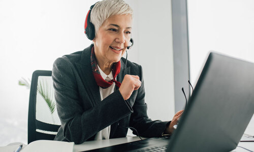 Eine Frau sitzt mit einem Headset vor dem Laptop.