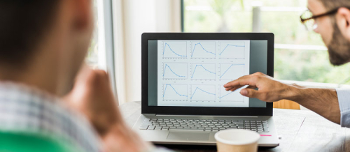 ein Mensch zeigt einem anderem Menschen etwas am Bildschirm eines Computersm Computer