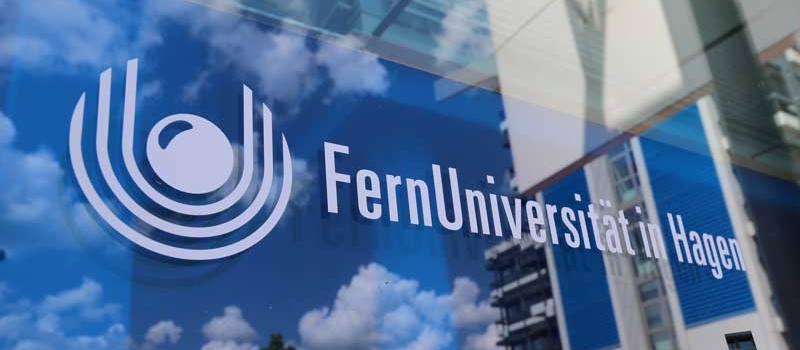 FernUni-Logo auf Glasscheibe (mit Spiegelung von Wolken und dem AVZ-Gebäude im Anschnitt)