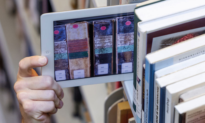 Hand zieht Tablet aus dem Bücherregal (Bibliothek)