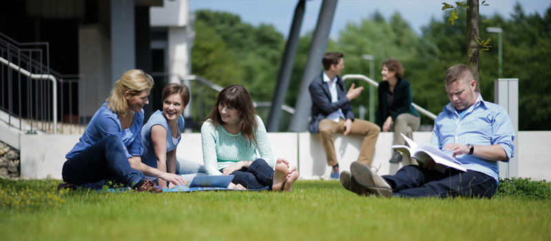 Vier Studierende sitzen auf der Wiese des Campus der FernUniversität Hagen