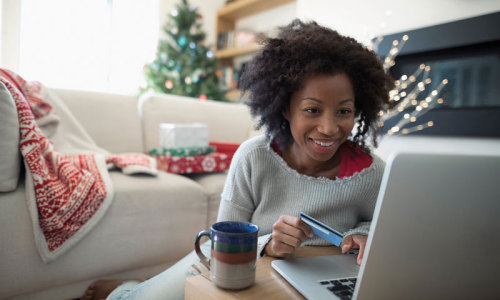 Frau am Notebook im Wohnzimmer, mit Kaffeetasse, im Hintergrund ein Weihnachtsbaum