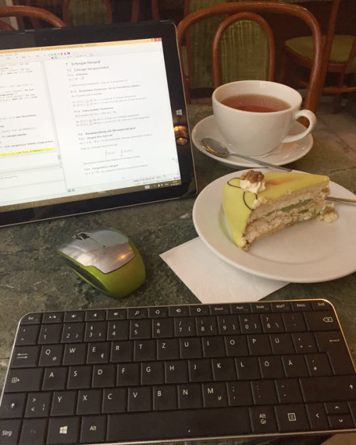 Ein Laptop liegt auf einem Tisch im Cafe, daneben stehen eine Tasse Tee und ein Stück Kuchen.