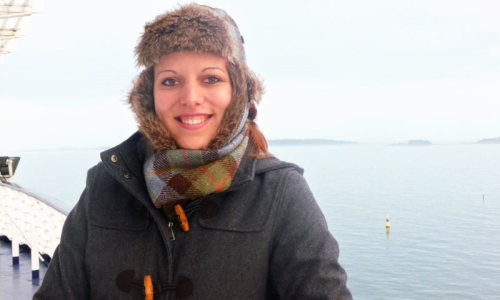 Eine Frau in Wintermantel und mit Mütze steht auf einem Schiffsdeck.
