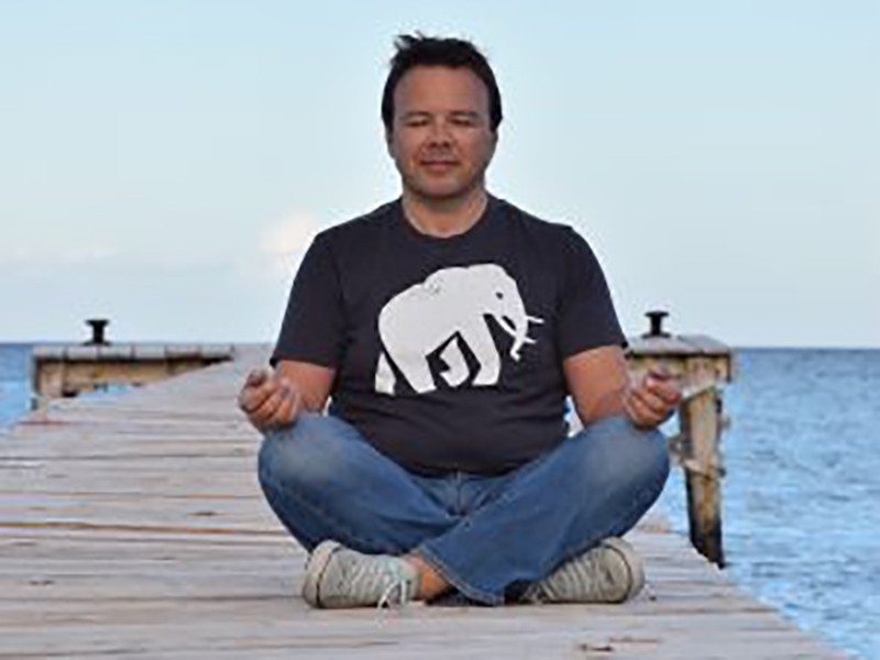 ein Mann sitzt in Meditationshaltung auf einem Steg am Wasser