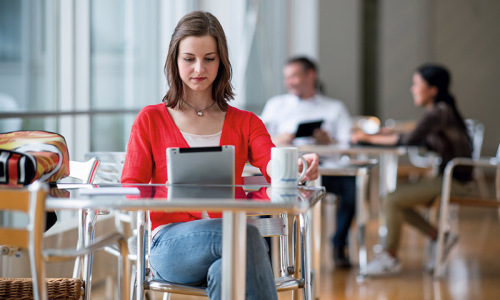 Eine Frau sitzt an einem Tisch und blickt konzentriert auf ihren Tablet-PC.