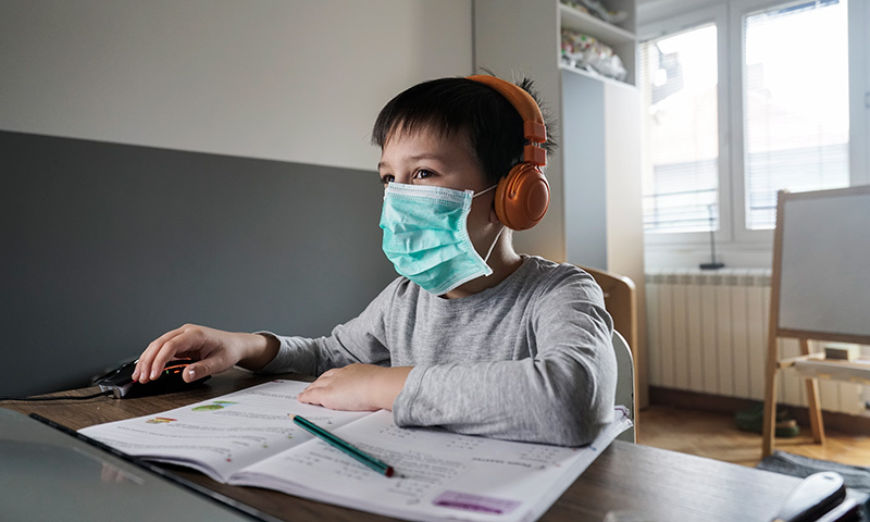 Kind mit Maske vor einem Computer un dmit Schulheft