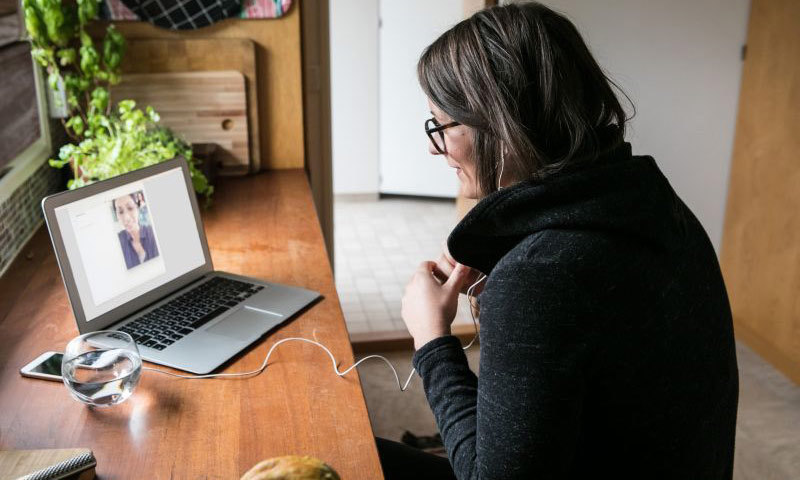 Eine Frau sitzt vor einem Laptop und spricht mit einer anderen Frau auf dem Display.