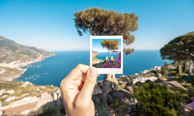 Hand holding a polaroid photo of a landscape in front of the same landscape