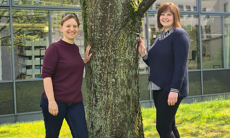 Zwei Frauen stehen an einem Baum im Grünen