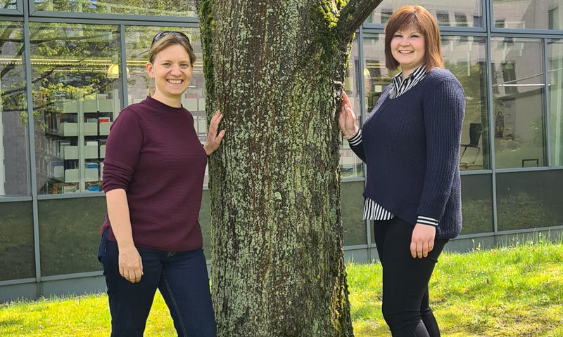 Zwei Frauen stehen an einem Baum hinter der Universitätsbibliothek Hagen.