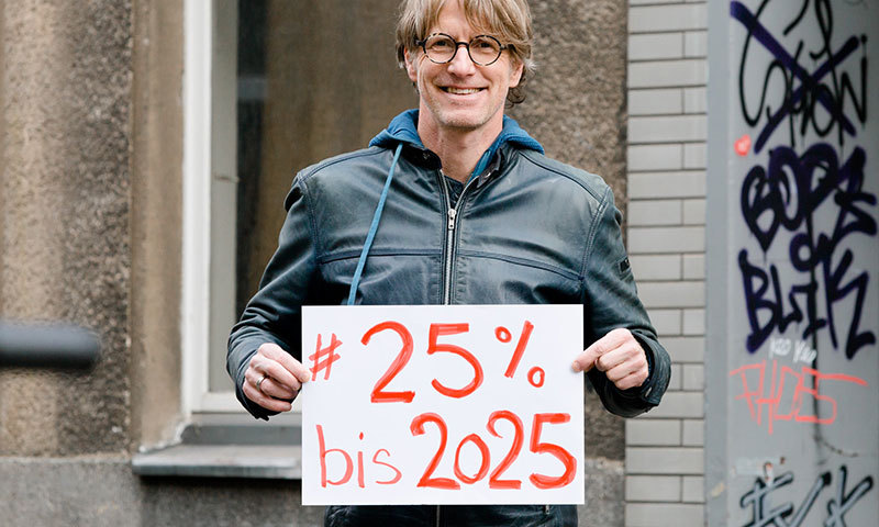 Ein Mann hält ein Schild fest, auf dem steht: 25 Prozent bis 2025.