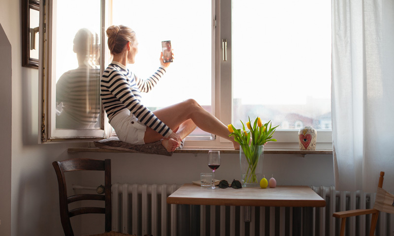 Frau mit Smartphone am offenen Fenster