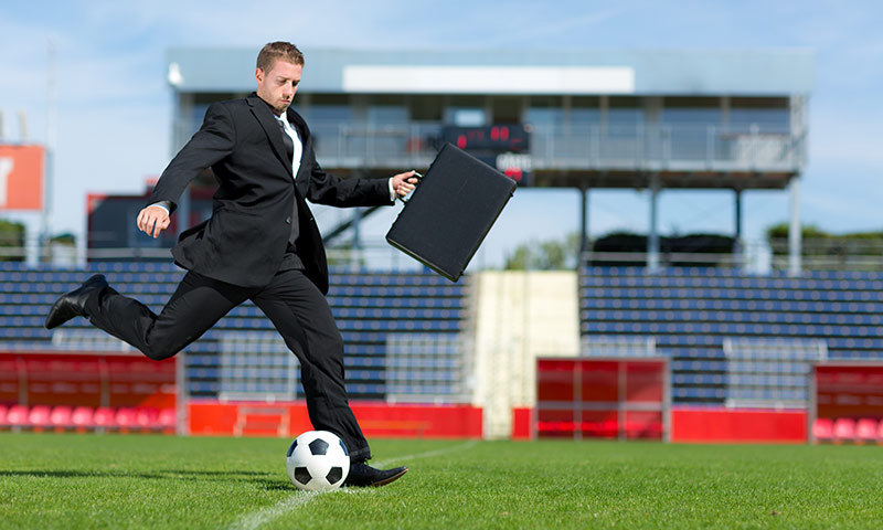 ein Mann im  Business-Dress spielt Fußball im Stadion