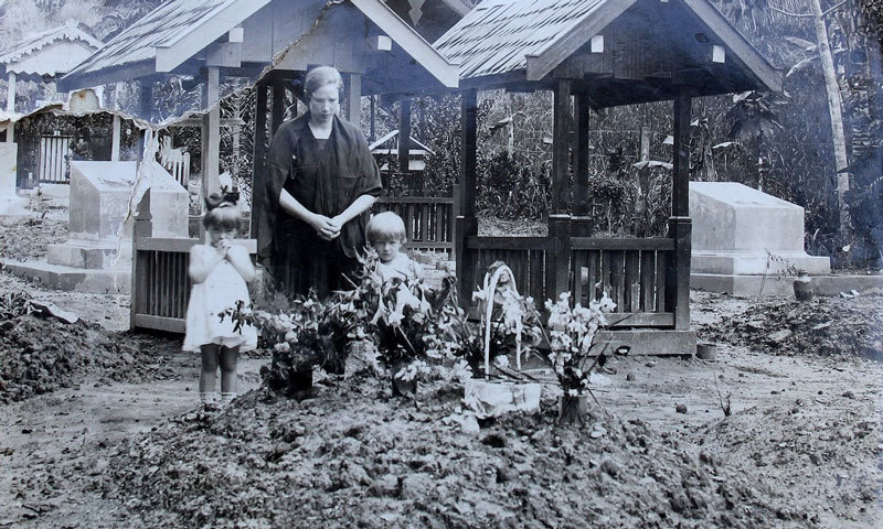 Frau mit zwei Kindern blickt auf Grab