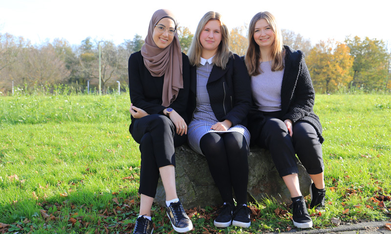 Drei Frauen sitzen im Grünen auf einem Stein