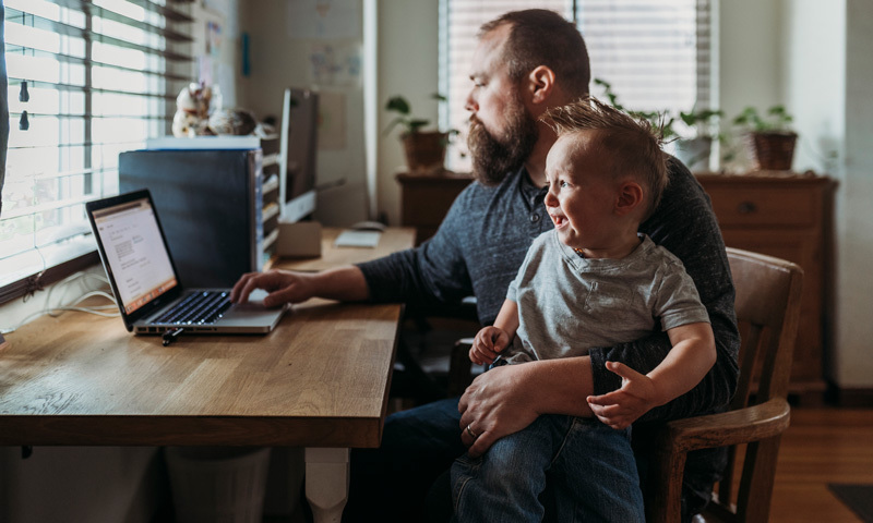 Vater mit Sohn auf dem Schoß, arbeitet am Laptop