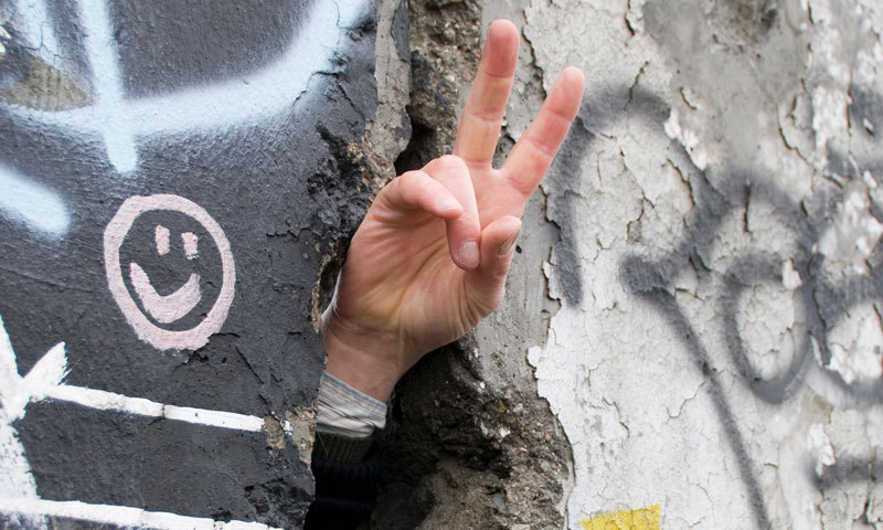 Finger mit Peace-Zeichen durch Mauerloch