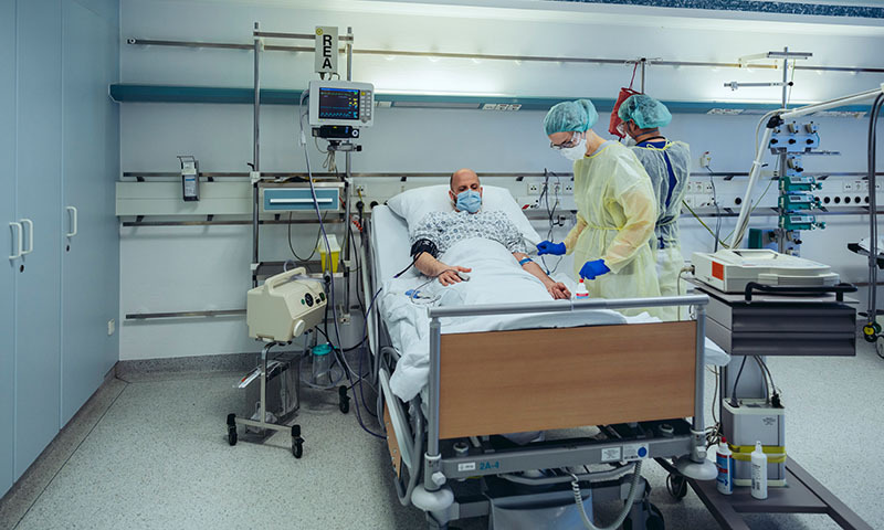 Mann in Krankenhausbett mit zwei Pflegenden 