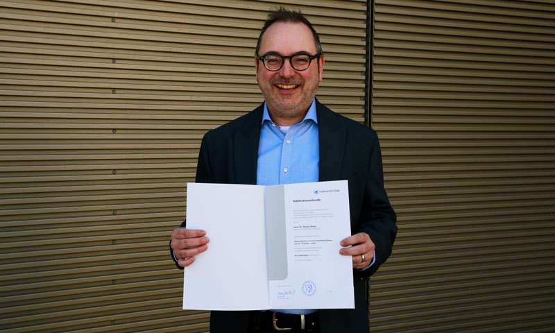 Mann hält eine Urkunde in der Hand.