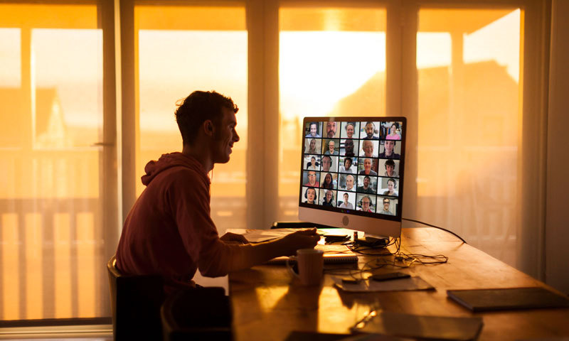 Mann sitzt vor einem PC. Auf dem Bildschirm findet eine Online-Veranstaltung statt. 