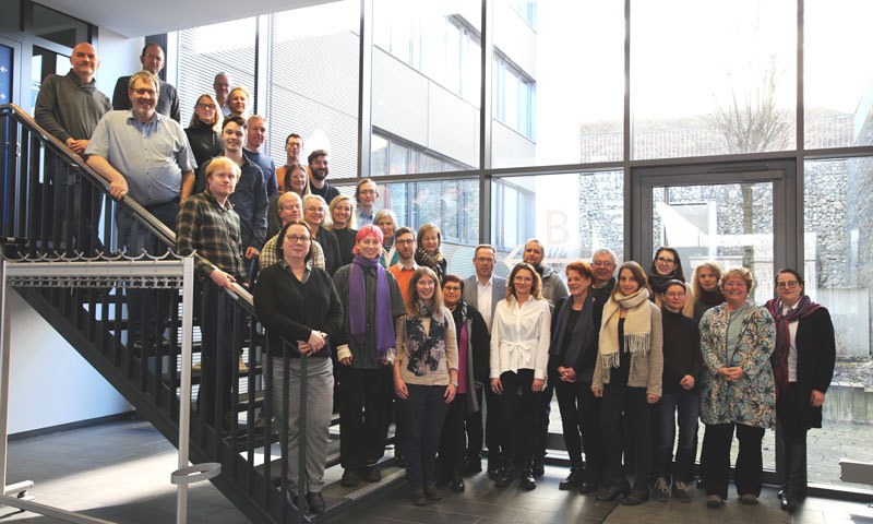 Eine Gruppe von Archivarinnen und Archivaren steht vor einer Treppe für ein Gruppenfoto zusammen. 