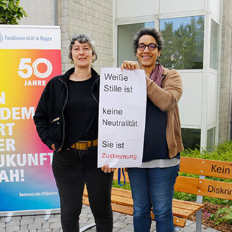 Fatia Pindra (re.), Teamassistentin in den Fakultäten für Kultur- und Sozialwissenschaften sowie für Wirtschaftswissenschaft. Zitat auf Tafel: Weiße Stille ist keine Neutralität. Sie ist Zustimmung