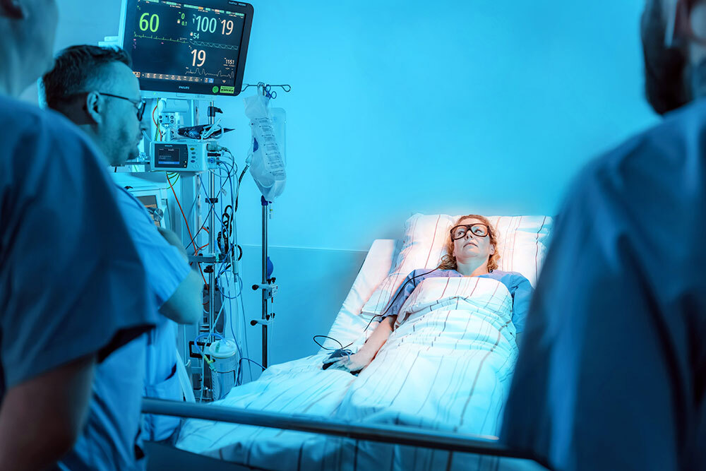 Ärzte stehen in einem Krankenhauszimmer um das Bett einer Patientin, die eine Eyetracking-Brill trägt.