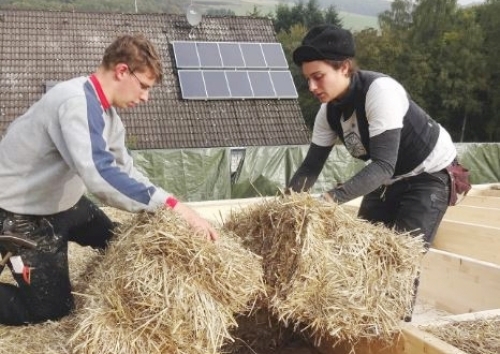Zwei Zimmerleute bauen Strohballen in ein flachgeneigtes Dach ein.