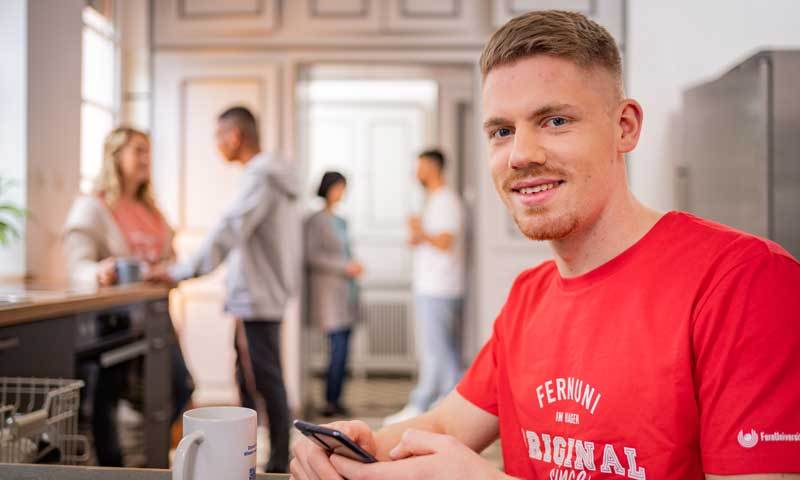 Mann sitzt mit einem Smartphone an einem Küchentisch. 