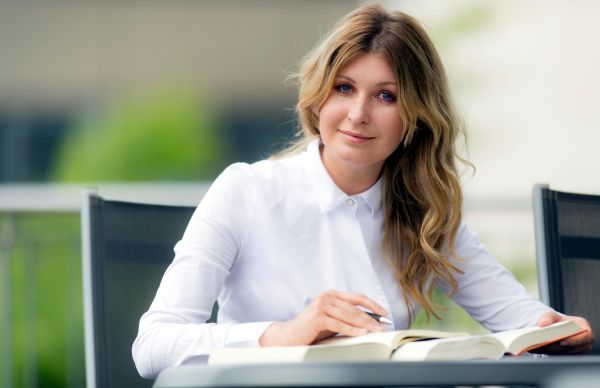 Eine Frau sitzt am Tisch. Vor ihr liegt ein aufgeschlagenes Buch.