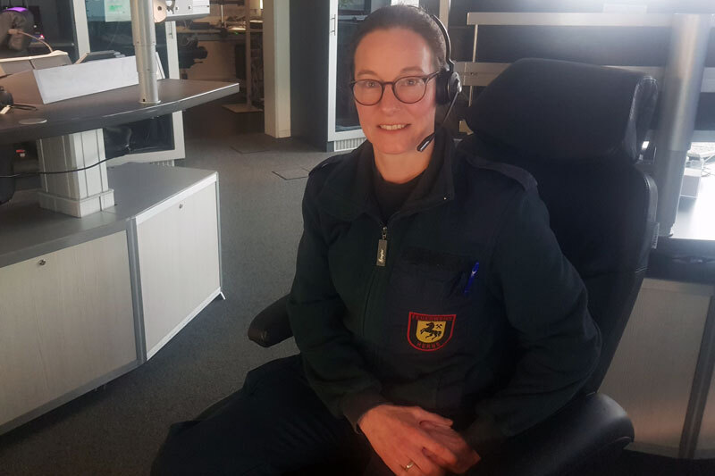 Eine Frau sitzt in einer Leitstelle, sie trägt ein Headset, um Anrufe entgegennehmen zu können.