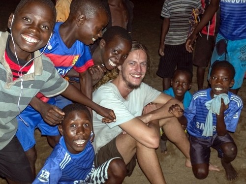 Ein junger Mann ist umgeben von Nachbarskindern am Malawisee in Afrika.