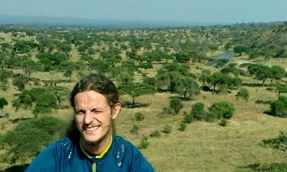 Blick auf eine Savanne im afrikanischen Malawi mit Bäumen und Steppe, im Vordergrund steht ein junger Mann.
