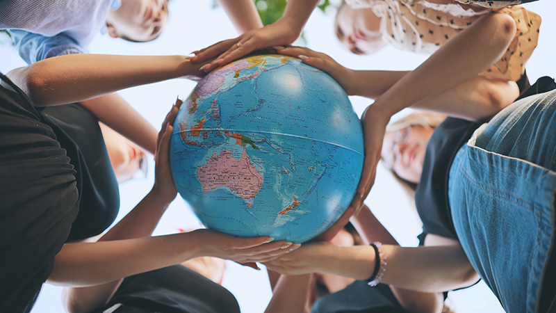 Junge internationale Menschen halten einen Globus gemeinsam