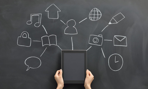 Chalkboard with a network of drawn objects and hands holding a tablet