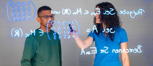 Zwei Studierende arbeiten an einem Lightboard mit einer mathematischen Formel.