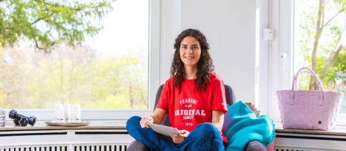 Eine Frau sitzt auf einem Stuhl und hält einen Studienbrief in der Hand.