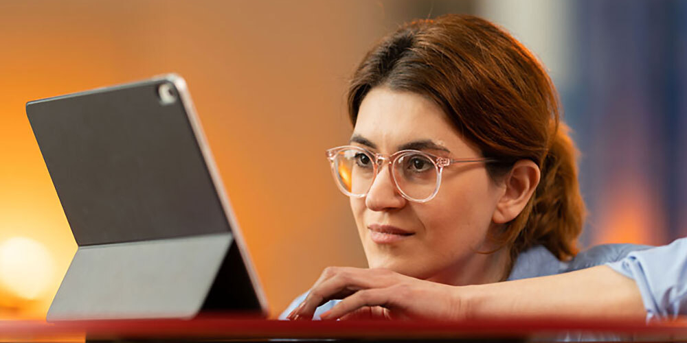 Woman wearing glasses looking intently at a tablet on a table