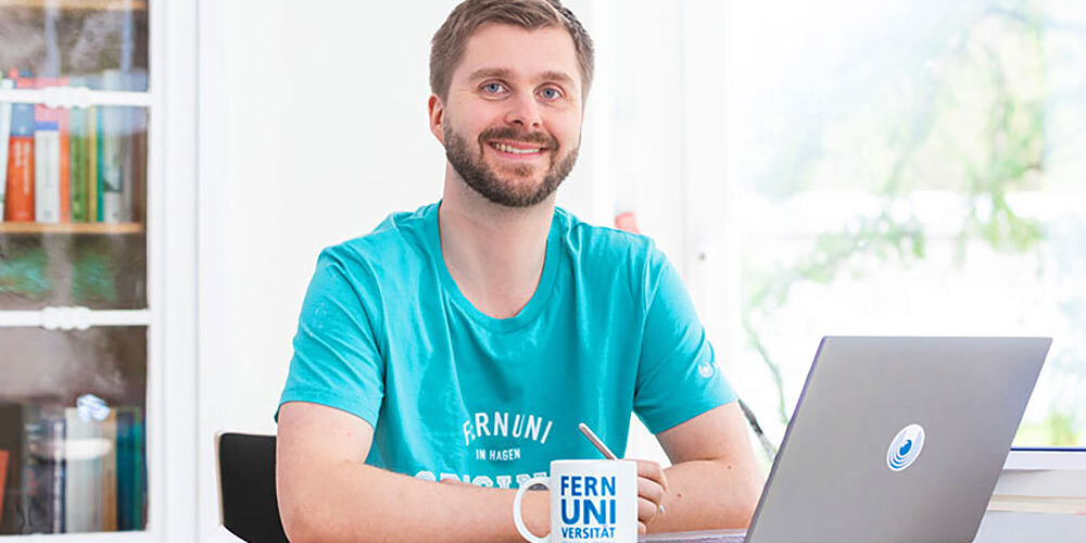 Young man with beard sitting at a table with laptop and mug