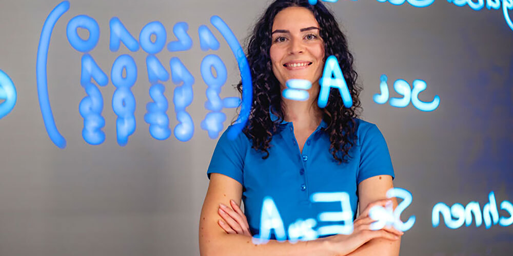 Woman with crossed arms standing in front of a glass wall with mathematical formulas in blue writing