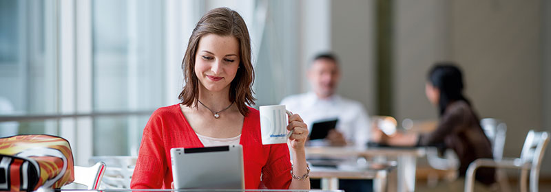 junge Frau sitzt mit Tablet und FernUni-Tasse am Tisch