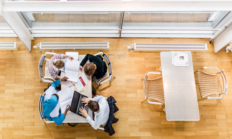 Vier Student:innen am Tisch mit Laptop und aufgeschlagenen Büchern aus der Vogelperspektive